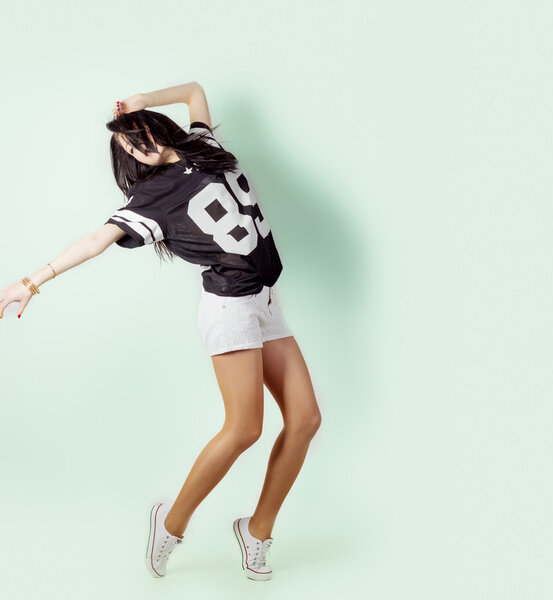 Молодая энергичная спортивная активная девушка танцует в Студии на светлом фоне в футболках и шортах
