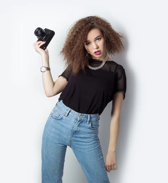 Beautiful young hipster girl holding the camera makes images, photos on the camera, in jeans and a black t-shirt in the Studio — Stock Photo, Image