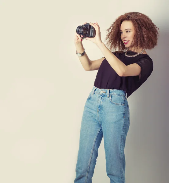 Mooi meisje hipster maakt de beelden, de foto's op de camera in spijkerbroek en een zwart t-shirt in de Studio — Stockfoto