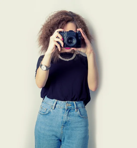 Menina bonita hipster faz as imagens, fotografias na câmera em jeans e uma camiseta preta no Estúdio Fotografias De Stock Royalty-Free