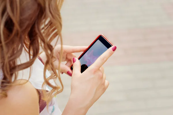 Bella ragazza con i capelli ricci in piedi sulla strada in telefono in mano, invia un messaggio SMS legge — Foto Stock