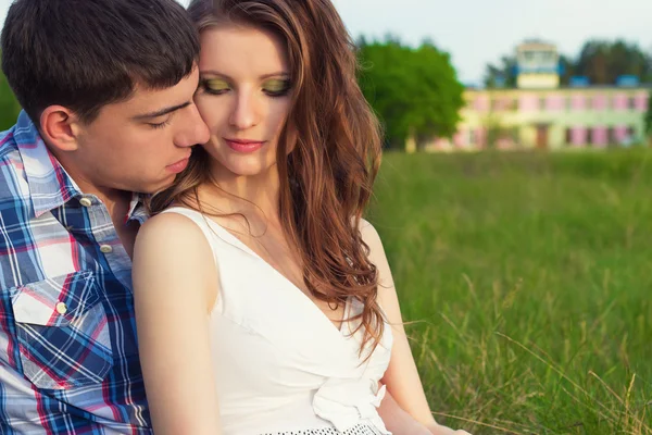 Young beautiful loving happy couple sitting in the box on the grass in the warm evening summer day — Stock Photo, Image