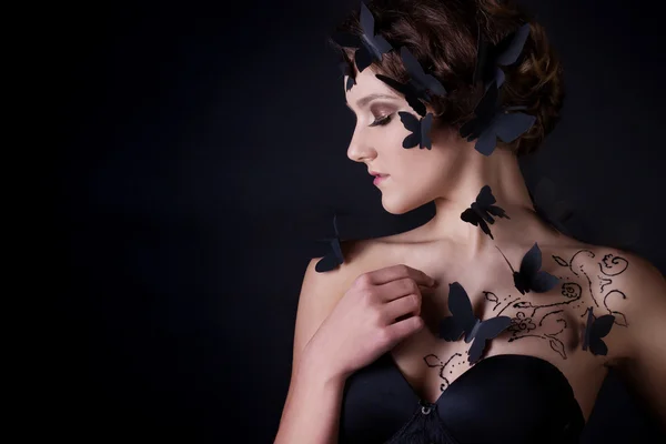 Fashion portrait of a beautiful girl in profile on a black background with black butterflies on the body — Stock Photo, Image