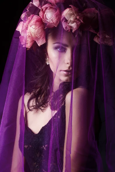 Menina sexy bonita com cabelo preto em um vestido de renda preta com uma coroa de flores em sua cabeça coberta com um véu violeta no estúdio em um fundo preto, retrato de beleza — Fotografia de Stock