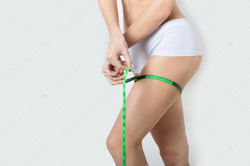 Young beautiful athletic girl measures thighs and legs measuring tape, healthy lifestyle, fitness, exercise, healthy slim body