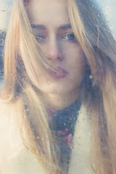 Beautiful cute tender young girl with big sad eyes with white hair and dark lipstick in a bright coat looks into the camera through wet glass — Stock Photo, Image