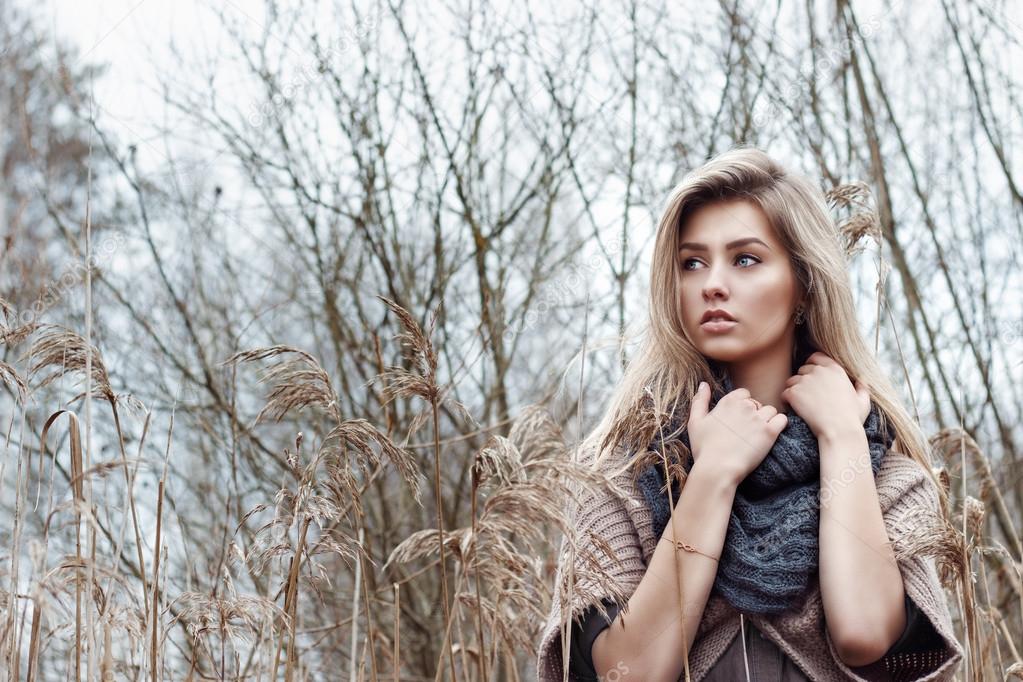 Portrait of a beautiful girl with blue eyes in a grey jacket in the field among trees and tall dry grass, tinted in shades of gray