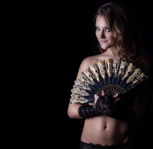 Beautiful sexy girl in black lingerie with curls and bright make-up with a fan in his hand and a smile on your face on a black background in Studio — Stock Photo, Image