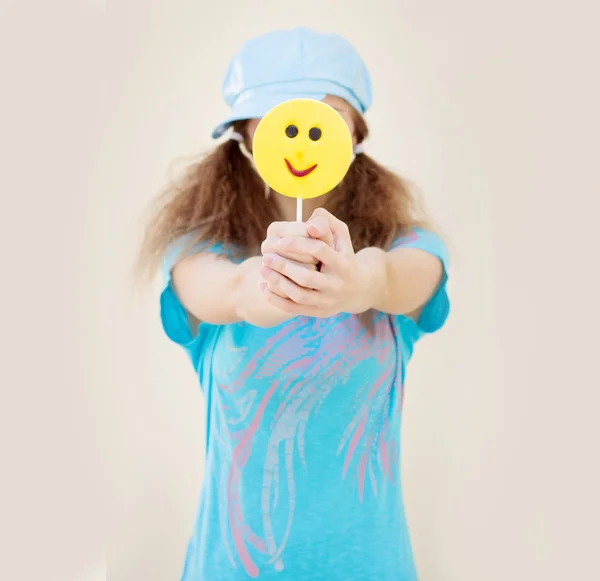 Chica de camisa azul y gorra con dos colas sostiene delante de un gran caramelo amarillo —  Fotos de Stock