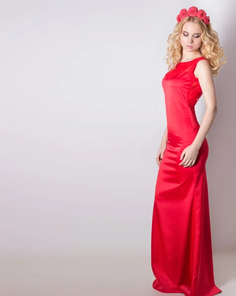 Сексуальная девушка в красном длинном вечернем платье с цветами в волосах и завитой прической — стоковое фото