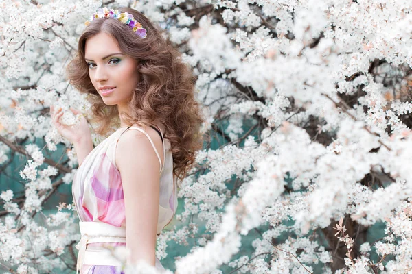 Елегантна красива дівчина з пишним волоссям з обідком яскраво-кольорових квітів в саду біля квітучого дерева теплий весняний ранок — стокове фото