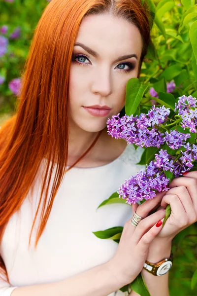 Bela mulher sexy com cabelo regime de fogo com olhos de uma raposa no jardim com lilases — Fotografia de Stock