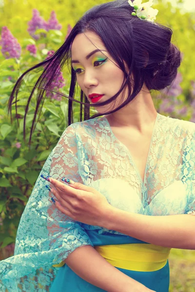 China hermosa chica sexy en un kimono con un hermoso maquillaje con el pelo caminando en un jardín cerca de arbustos de color lila floreciente —  Fotos de Stock