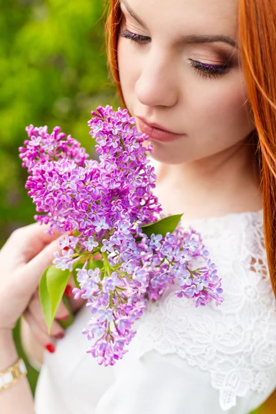 Красивая сексуальная женщина с огненно-рыжими волосами в саду с сиренью и белым платьем с красивым макияжем — стоковое фото