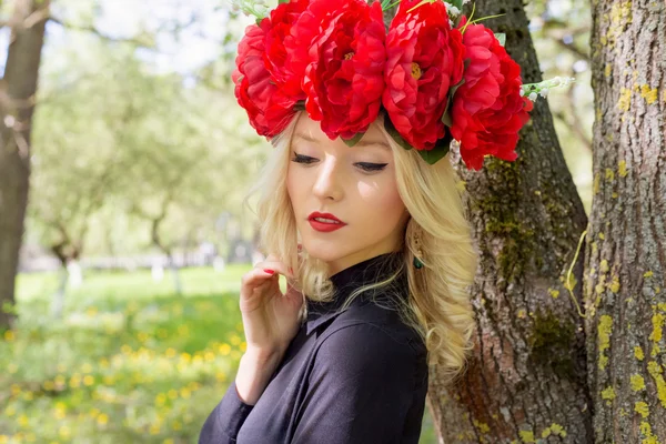 Porträtt av vacker sexig blond tjej med en krans av pion promenader i trädgården på en solig dag — Stockfoto