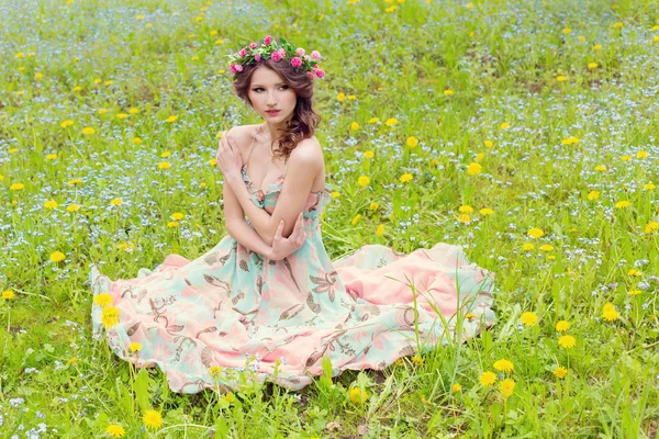 Bela menina macia sexy em um vestido de verão e com uma grinalda em sua cabeça sentado no prado de flores azuis — Fotografia de Stock