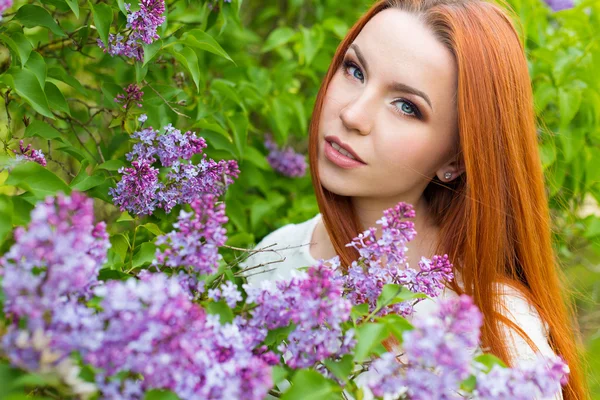 Bella ragazza dai capelli rossi sexy carino con i capelli lunghi in un abito bianco con un mazzo di lilla nelle mani di — Foto Stock