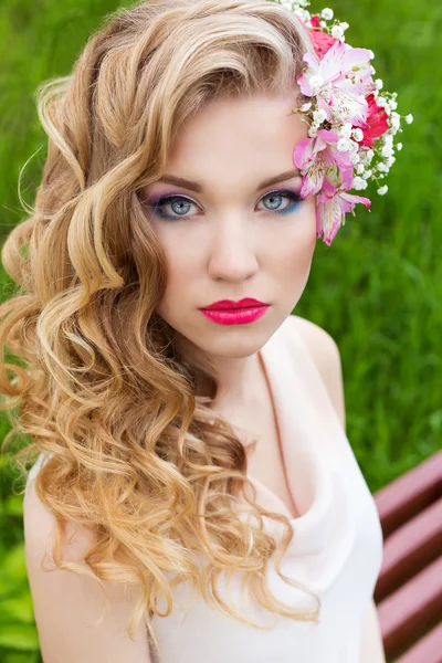 Beautiful tender sweet girl in a white dress with a wedding hairdo curls bright makeup and red lips with flowers in her hair — Stock Photo, Image