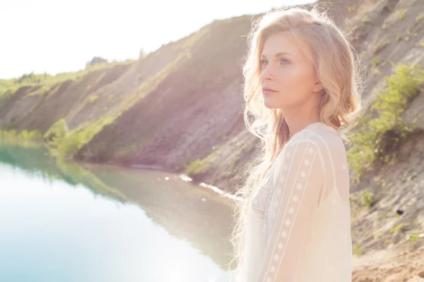 Piękna dziewczyna jasny miękkie z blond włosy faliste stoi na brzegu jeziora na zachód słońca na jasny, słoneczny dzień — Zdjęcie stockowe