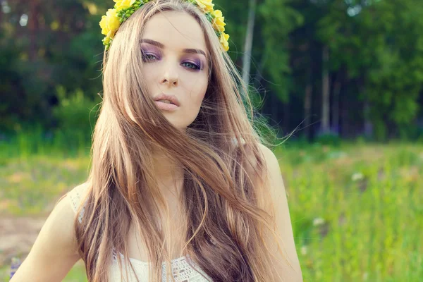 Beautiful sexy sweet girl with long hair and a wreath of yellow roses on his head in the field, the wind blowing her hair — Stockfoto