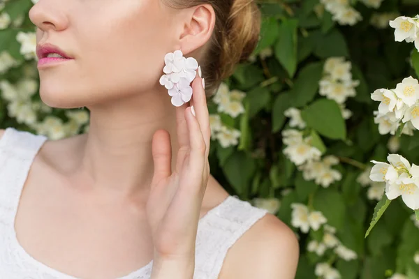 Beautiful sexy tender girl near blossoming tree exhibits beautiful delicate earrings in the form of flowers with rhinestones — Stock fotografie