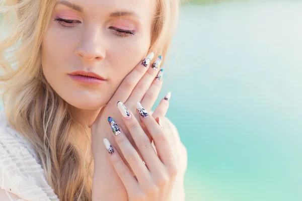 Beautiful sexy cute gentle blonde girl in a white dress holding hands near the face with long acrylic nails — Stockfoto