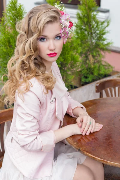 Bela menina doce com cabelo e cor de maquiagem brilhante sentado em uma mesa em um café ao ar livre e esperando por sua ordem — Fotografia de Stock