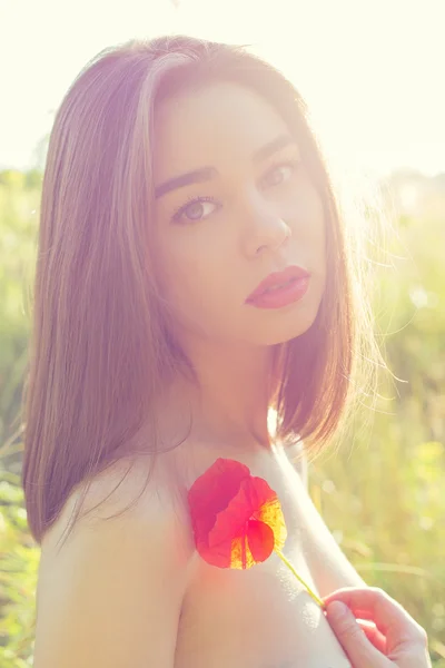 美丽性感的女孩与一朵罂粟花在手上露出肩膀在日落时的阳光下，字段中的丰满嘴唇在温暖的颜色底纹 — 图库照片