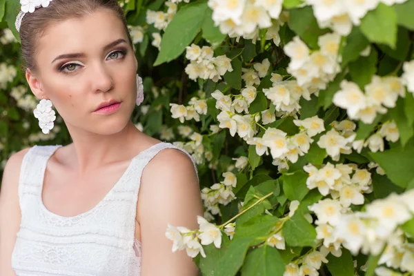 Vackra sexiga mild söt flicka brud i en vit klänning, med fina smink och hår, med örhängen från blommor och kristaller i ett blommande träd Jasmine — Stockfoto