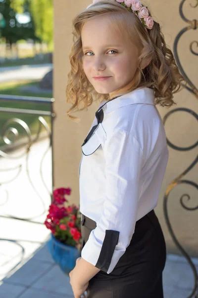 Beautiful sweet girl schoolgirl in school uniform outside on a sunny day with curly hair and a wreath of delicate roses in her hair — Stock Photo, Image