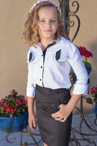 Beautiful sweet girl schoolgirl in school uniform outside on a sunny day with curly hair and a wreath of delicate roses in her hair — Stock Photo, Image