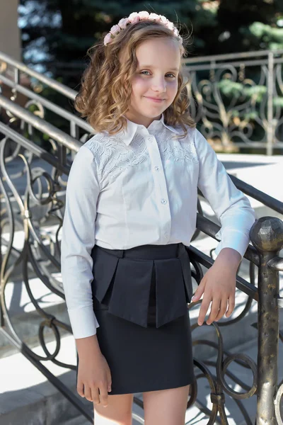 Beautiful sweet girl schoolgirl in school uniform outside on a sunny day with curly hair and a wreath of delicate roses in her hair — Stock Photo, Image