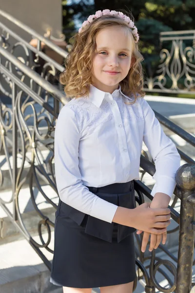 Beautiful sweet girl schoolgirl in school uniform outside on a sunny day with curly hair and a wreath of delicate roses in her hair — Stock Photo, Image