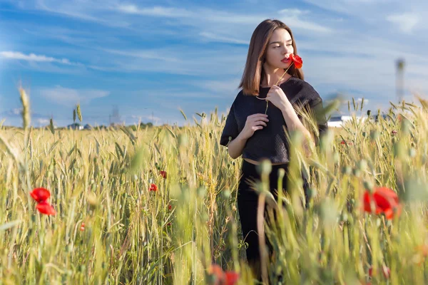 Beautiful sexy cute girl with big lips and red lipstick in a black jacket with a flower poppy standing in a poppy field at sunset on a sunny warm summer day — Stock Photo, Image