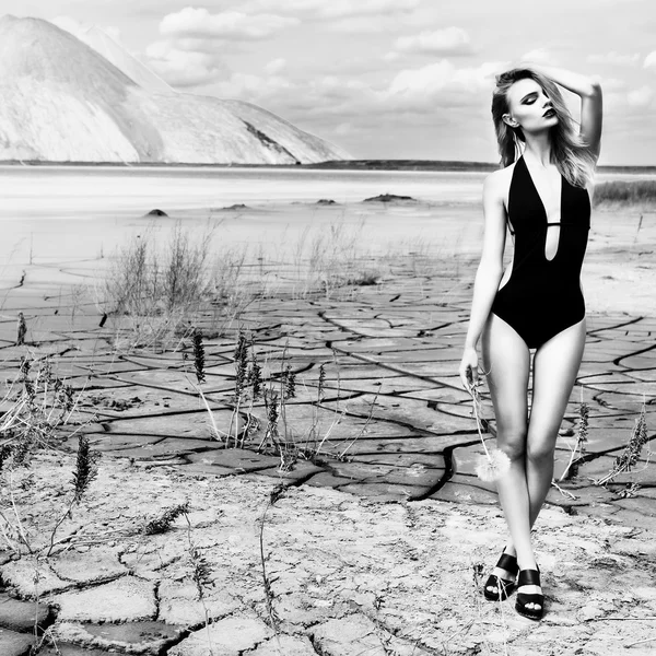 Belle fille mignonne sexy dans un tournage de mode dans un maillot de bain dans le désert terre fissurée sèche dans le fond des montagnes sous le ciel sur une journée d'été ensoleillée, modèle proportionnellement — Photo