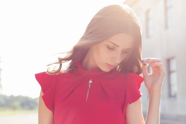 Beautiful sexy girl in a red dress with a gentle look into the sun at sunset in bright sunny day — Stock Photo, Image