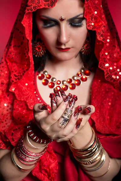 beautiful girl in the image of Indian woman in a red sari with beautiful patch acrylic nails in oriental style in the studio