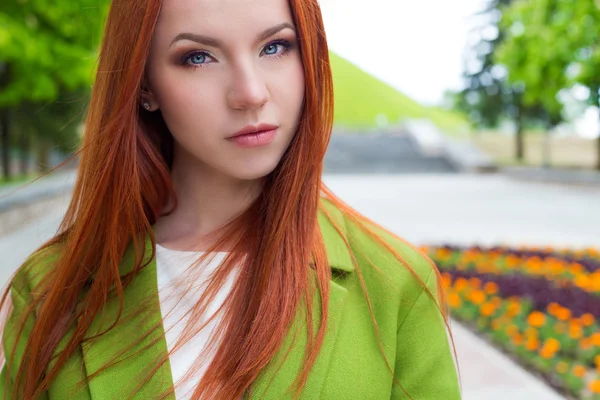 Beautiful sexy red-haired girl in a green coat walking in the park — Stock Photo, Image