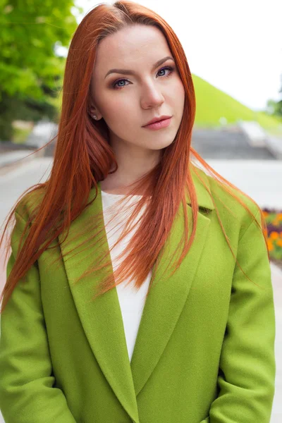 Belle fille sexy aux cheveux roux dans un manteau vert marchant dans le parc — Photo