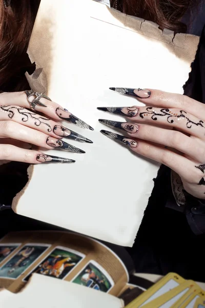 Piękne dłonie z długim akrylowe czarownica czarny paznokcie, trzymając w rękach arkusz biały — Zdjęcie stockowe