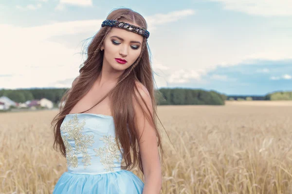 Hermosa chica sexualintelligance modelo en vestido azul con diseño de labios rosados demuestra un borde en la cabeza en un campo en un día soleado —  Fotos de Stock