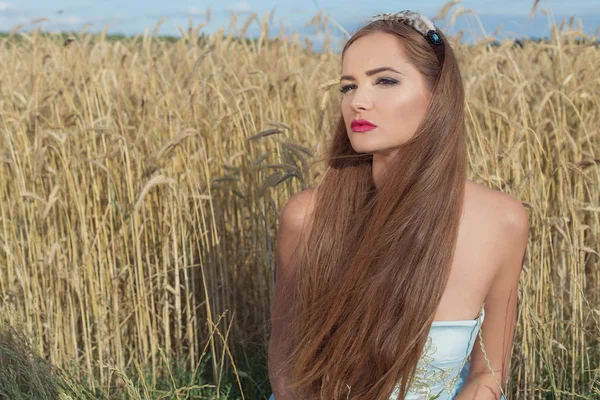 Hermosa chica sexualintelligance modelo en vestido azul con diseño de labios rosados demuestra un borde en la cabeza en un campo en un día soleado — Foto de Stock