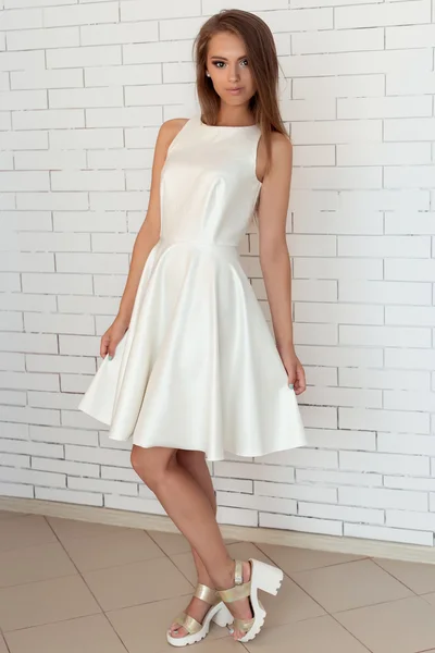 可爱漂亮的女孩穿着白色连衣裙在明亮时尚鞋在工作室里的砖壁附近 — 图库照片