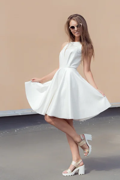 Ziemlich süßes schönes Mädchen in einem strahlend weißen Kleid in modischen Schuhen und Sonnenbrille, die sich auf dem Dach dreht — Stockfoto