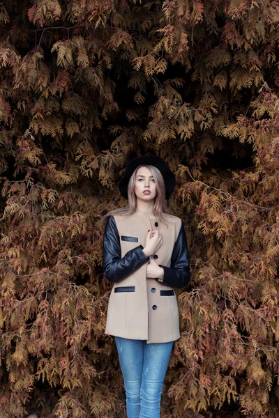 Attractive slender beautiful sad girl in a black hat and coat is dried under a yellow tree in autumn Park — Stock Photo, Image