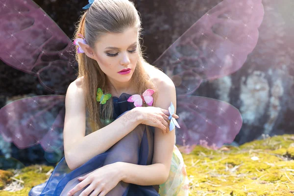 Bela sexy bonito menina elfo borboleta senta-se em uma clareira na floresta na luz do sol com borboletas em seu cabelo e braço com maquiagem brilhante — Fotografia de Stock