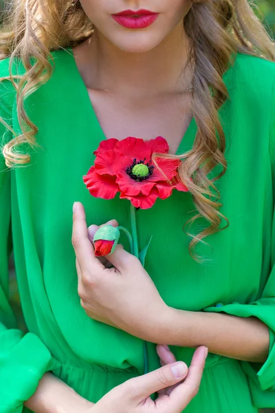 Vacker sexig kvinna med röda läppar och ljusa make-up i en grön klänning med en vallmo i händerna i en skog — Stockfoto