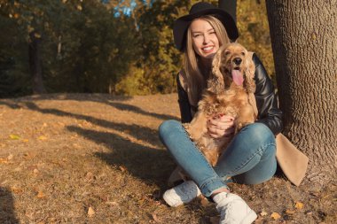 Köpeğini bir parkta ile sonbaharda başka oynarken siyah şapkalı güzel şirin mutlu kız güneşli bir gün