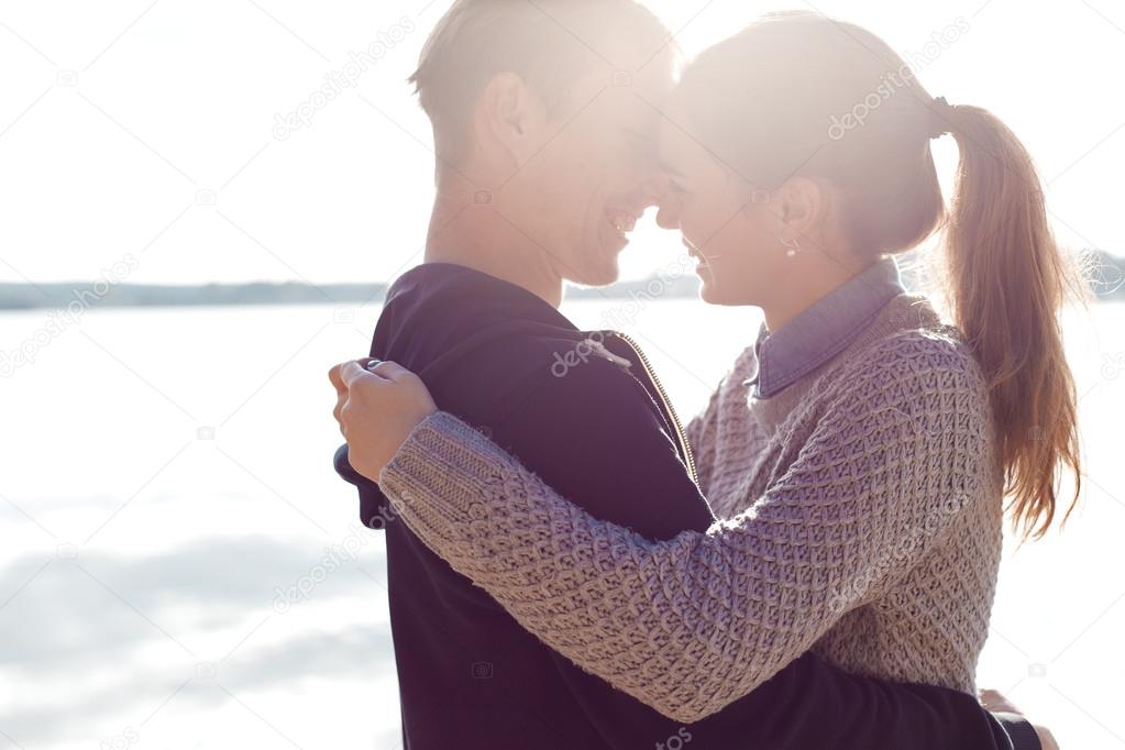 Beautiful young couple in love walking on the shore of the lake at sunset in the rays of bright light