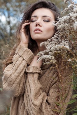 beautiful sad cute attractive woman in a beige sweater wide in a field of dry grass in autumn cold overcast day, photo of beige brown tones, chocolate hues